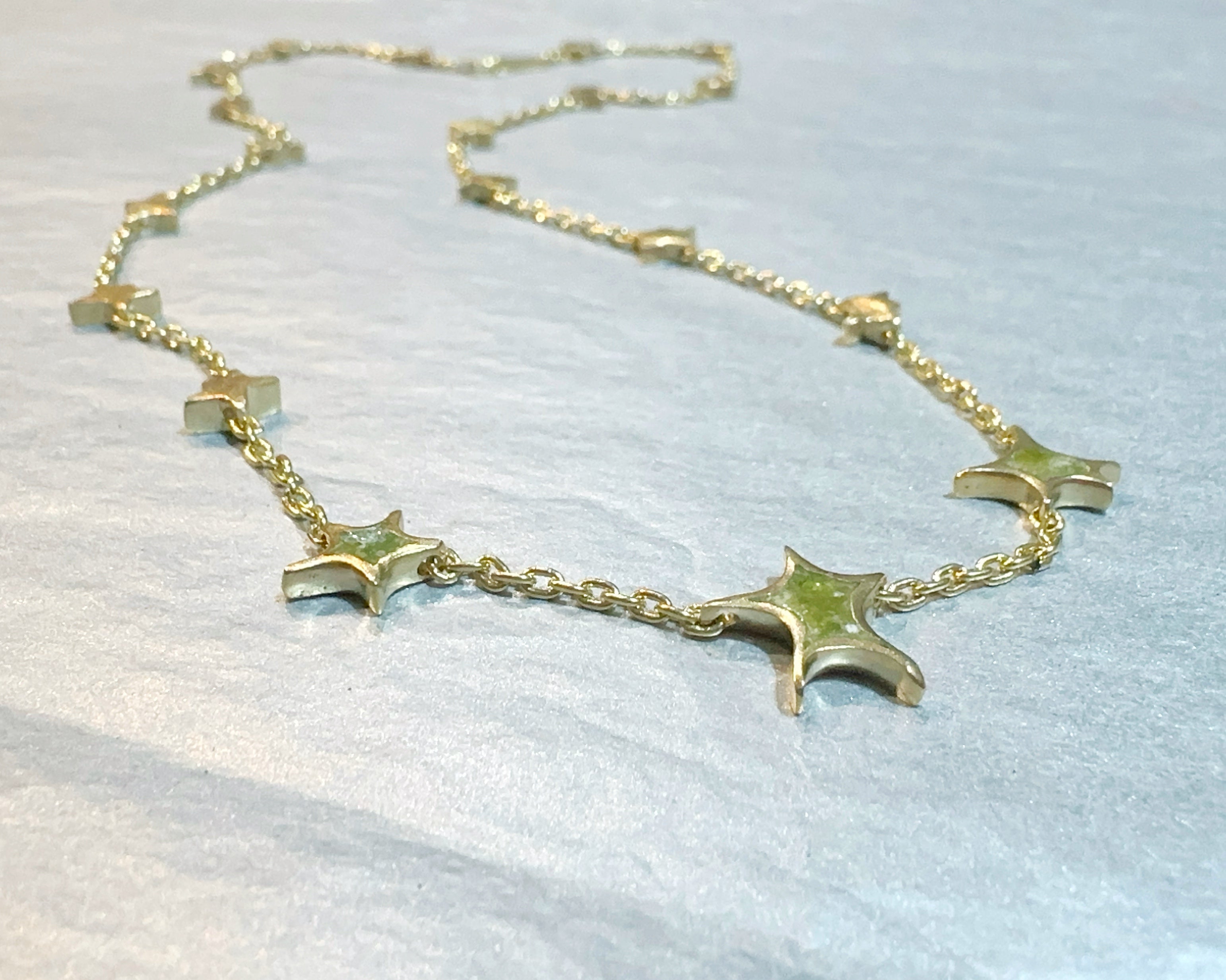 Gold necklace with star-shaped pendants on a light blue fabric background