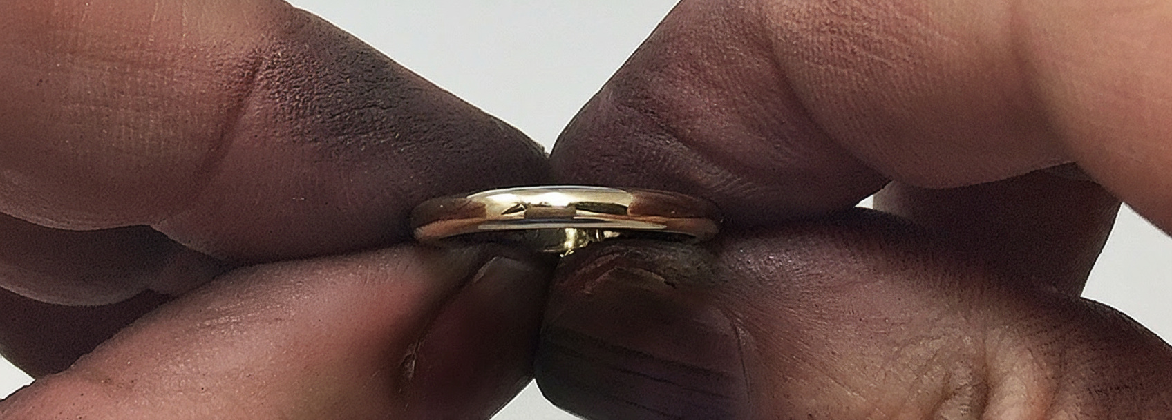Gold ring being held between two fingers against a neutral background